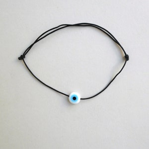 Puede incluir: Un brazalete de cuerda negra con un dije de ojo turco azul y blanco.