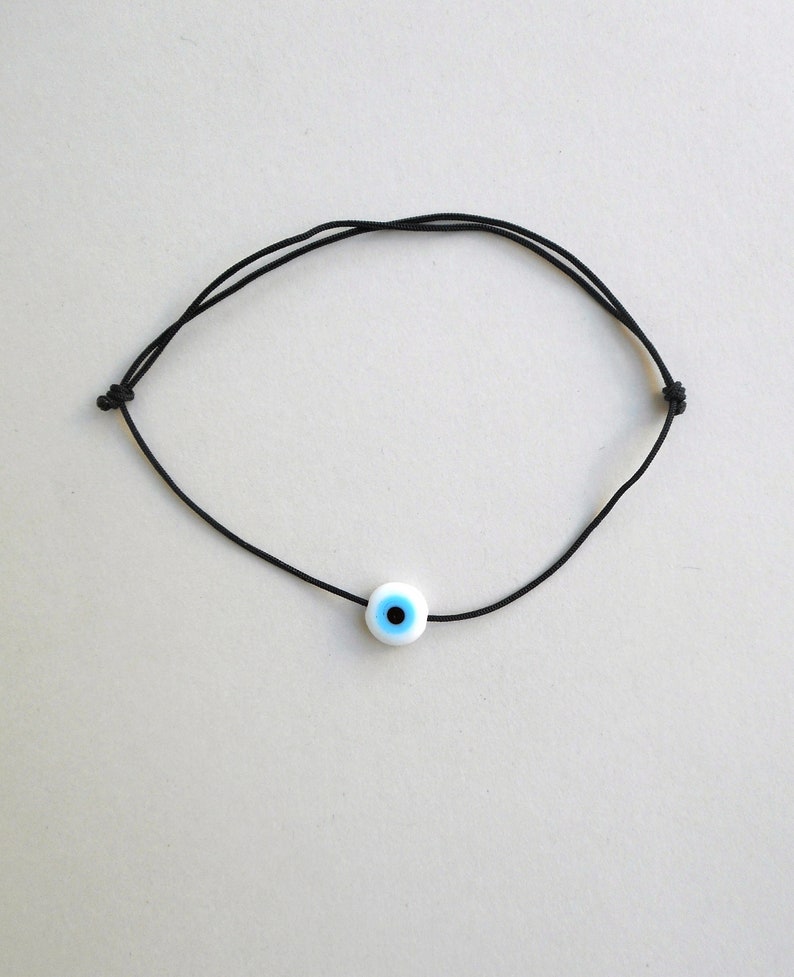 Puede incluir: Un brazalete de cuerda negra con un dije de ojo turco azul y blanco.