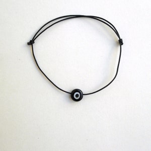 Puede incluir: Un brazalete de cuerda negro con un dije de ojo turco negro y blanco.