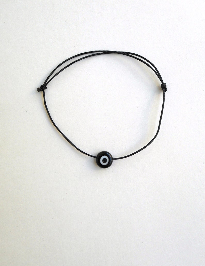 Puede incluir: Un brazalete de cuerda negro con un dije de ojo turco negro y blanco.