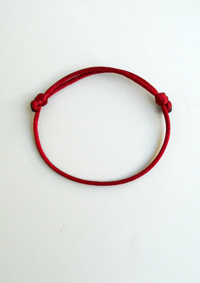 K&ouml;nnte beinhalten: Ein rotes Armband aus Schnur mit schwarzen Knoten an jedem Ende.