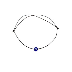 Puede incluir: Un collar sencillo de cord&oacute;n negro con un dije azul de ojo turco.