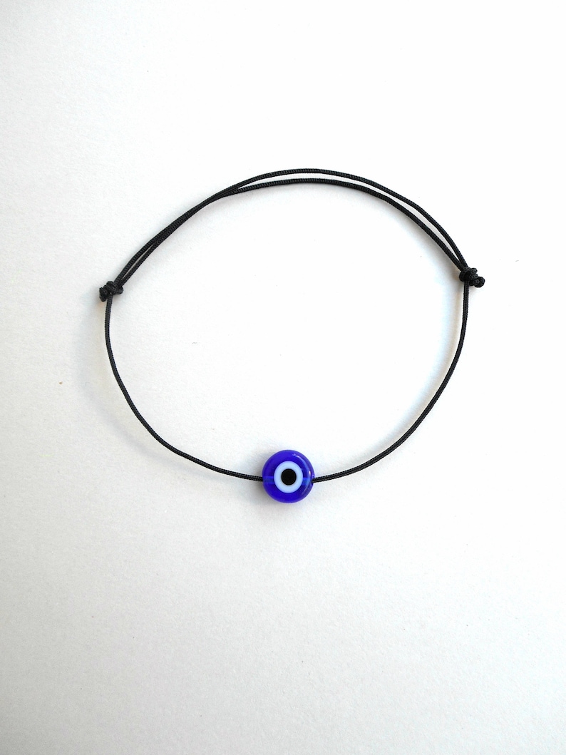 Puede incluir: Un brazalete de cuerda negra con un dije azul de ojo turco.