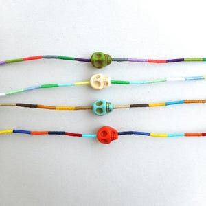May include: Four colorful bracelets with skull beads. Each bracelet has a different colored skull bead: green, white, blue, and orange. The bracelets are made with colorful threads.