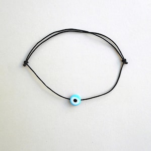 Puede incluir: Un brazalete de cuerda negra con un dije de ojo turco azul y blanco.
