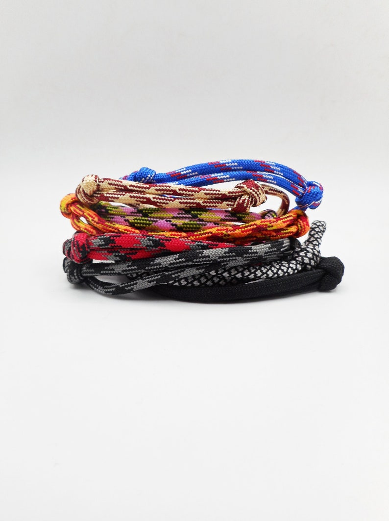 May include: A stack of six woven cord bracelets featuring various patterns and colors, including solid black, black and white, red and black, orange and yellow, green and pink, and blue with white accents, each secured with a simple knot closure.