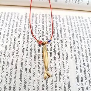 May include: A gold-colored fish pendant necklace with a red, white, and blue beaded charm. The necklace is on a red cord.