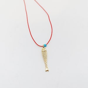 Peut inclure: Un collier avec un pendentif en forme de poisson doré sur un cordon rouge avec une perle turquoise.