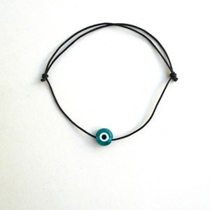 Puede incluir: Un brazalete de cuerda negra con un dije azul de ojo turco.