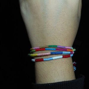 May include: A wrist with a colorful woven friendship bracelet. The bracelet is made of multiple strands of thread in various colors, including red, blue, green, yellow, and pink.