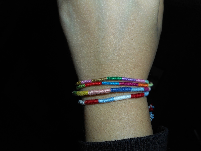 May include: A wrist with a colorful woven friendship bracelet. The bracelet is made of multiple strands of thread in various colors, including red, blue, green, yellow, and pink.