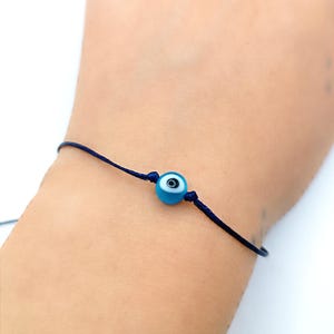 May include: A blue evil eye charm bracelet with a dark blue string.
