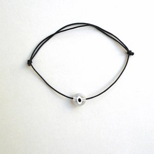 Puede incluir: Un brazalete de cuerda negro con una cuenta de ojo turco blanco y negro.