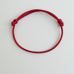 K&ouml;nnte beinhalten: Ein rotes Armband aus Schnur mit zwei Knoten an den Enden.