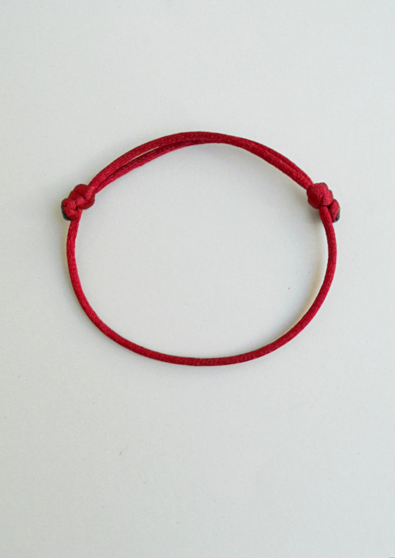 K&ouml;nnte beinhalten: Ein rotes Armband aus Schnur mit zwei Knoten an den Enden.