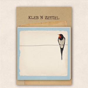 Könnte beinhalten: Ein Notizblock mit hellblauem Rand und einer Vogelillustration auf einem Draht. Der Vogel hat eine rote Kehle und einen schwarz-weiß gemusterten Körper. Der Notizblock hat oben den Text "KLEB 'N ZETTEL".