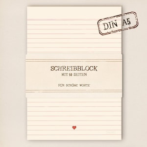 Könnte beinhalten: Cremefarbener Notizblock mit roten horizontalen Linien und dem Text "SCHREIBBLOCK" und "FÜR SCHÖNE WORTE". Ein rotes Herz befindet sich unten, und ein "DIN A5" Stempel befindet sich in der oberen rechten Ecke. Der Notizblock hat 50 Seiten.