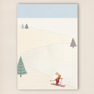 Könnte beinhalten: Notizblock mit hellblauem Header und einer skurrilen Illustration eines Ski fahrenden Kaninchens in roter Kleidung. Der Hintergrund zeigt eine verschneite Landschaft mit Bäumen und einem Rastermuster.