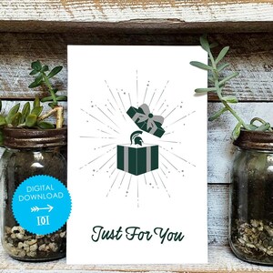 May include: White greeting card with a green gift box design, a Spartan helmet, and the text "Just For You." The card has a digital download label. The image is flanked by two glass jars with plants.