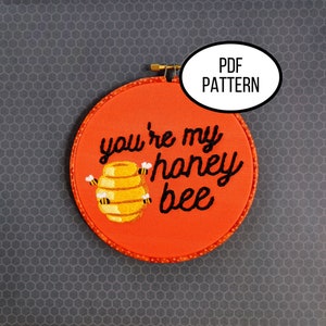 May include: A red embroidery hoop with the text "you're my honey bee" in black cursive font. A yellow and black beehive with bees is embroidered in the center.