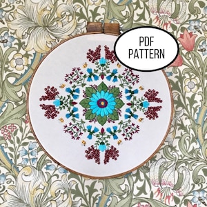 May include: A white embroidery hoop with a colorful floral design. The design features a blue flower with a yellow center, surrounded by red and green leaves and small yellow bees. The text "PDF PATTERN" is written in black on a white oval.