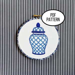 May include: A blue and white embroidered ginger jar design on white fabric, framed in a wooden hoop. The hoop is surrounded by a blue and white patterned fabric. The text "PDF PATTERN" is in a white oval.