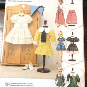 May include: Simplicity doll clothes pattern featuring various doll dresses. The pattern includes a yellow dress with white polka dots, a white dress with a blue bow, and other doll dress designs. The pattern is designed for dolls 18 inches (45.5cm) tall.