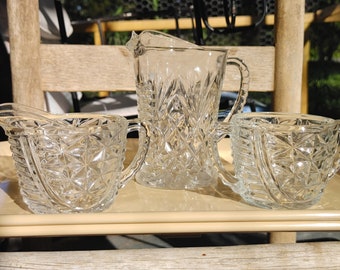 May include: A set of three clear glass serving pieces with a cut glass design. The set includes a jug, a creamer, and a sugar bowl.