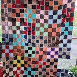 May include: A handmade quilt with a patchwork design. The quilt features a grid of squares in various colors and patterns, including red, blue, brown, and patterned fabrics. The squares are bordered by a neutral-colored fabric.