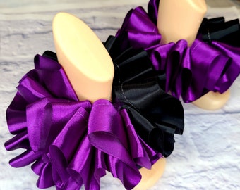 May include: A pair of purple and black satin leg warmers with ruffles. The leg warmers are made of multiple layers of satin ribbon.
