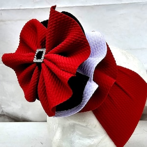 May include: A red, black, and purple fabric headband with a large red bow and a rhinestone accent.