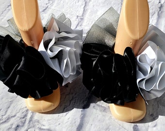 May include: A pair of black and white ruffled fabric shoe embellishments. The embellishments are made of black satin and white tulle.