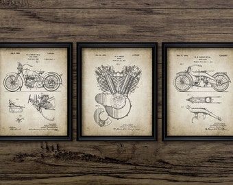May include: Three vintage black and white patent drawings of a motorcycle, engine, and motorcycle parts. The drawings are framed in black frames and are displayed on a wood background.