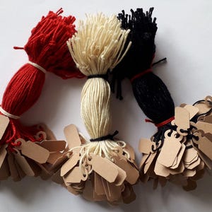 May include: Three bundles of yarn in red, cream, and black, each tied with twine and adorned with small, blank, brown tags. The yarn bundles are arranged in a semi-circle against a white background, suggesting a craft or DIY theme.