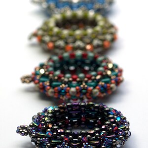 May include: Five beaded rings in various colors and patterns, including blue, green, red, and purple. The rings are stacked on top of each other, with the largest ring at the bottom and the smallest ring at the top. The rings are made of small beads that are woven together in intricate designs.