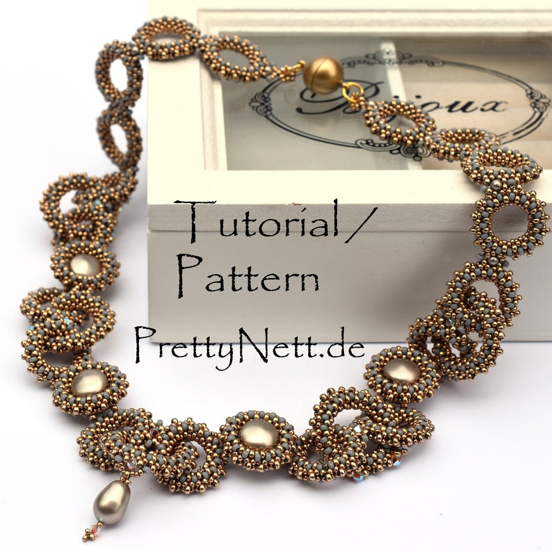 Może przedstawiać: Złoty i szary naszyjnik z perełką. Naszyjnik wykonany jest z małych koralik&oacute;w i ma delikatny, skomplikowany wz&oacute;r. Naszyjnik jest prezentowany w białym pudełku z tekstem "Tutorial/Wz&oacute;r PrettyNett.de".