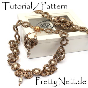 Może przedstawiać: Złoty i szary naszyjnik z koralik&oacute;w z delikatnym wzorem k&oacute;ł i pętli. Naszyjnik jest prezentowany na białym pudełku z tekstem "PrettyNett.de" na dole.