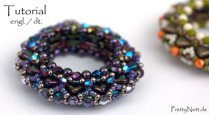May include: A close-up of a purple, blue, and silver beaded bracelet. The bracelet is made of small, round beads and is in the shape of a ring. The bracelet is on a white surface.