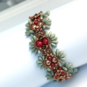 K&ouml;nnte beinhalten: Ein Armband mit Perlen in einem sich wiederholenden Muster aus gr&uuml;nen, roten und goldenen Perlen. Die Perlen sind in Herzform angeordnet.