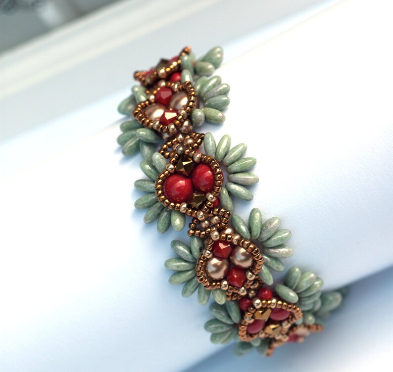 K&ouml;nnte beinhalten: Ein Armband mit Perlen in einem sich wiederholenden Muster aus gr&uuml;nen, roten und goldenen Perlen. Die Perlen sind in Herzform angeordnet.