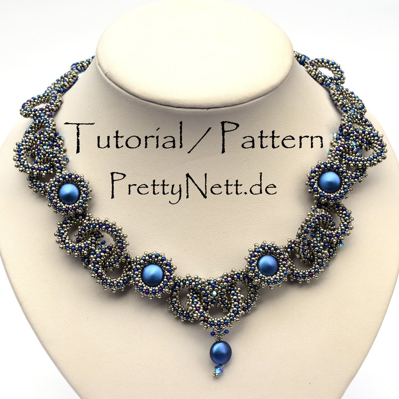 Może przedstawiać: Srebrny naszyjnik z niebieskimi koralikami z zawieszką. Naszyjnik ma powtarzający się wz&oacute;r małych koralik&oacute;w i większych niebieskich koralik&oacute;w. Zawieszka to pojedynczy niebieski koralik.