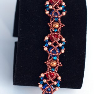 May include: A beaded bracelet with a copper wire design. The bracelet features red, blue, and gold beads in a geometric pattern.