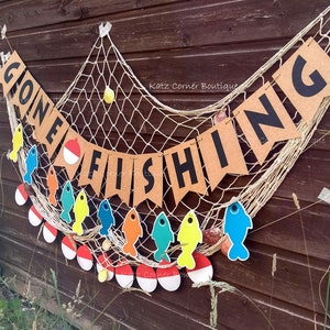 May include: A brown paper banner with the text "Gone Fishing" in black letters. The banner is strung on a white fishing net with colorful fish cutouts and red and white fishing bobbers.