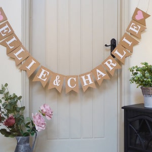 Pu&ograve; includere: Uno striscione in juta con i nomi "Ellie & Charlie" in lettere bianche e cuori rosa su ogni estremit&agrave;.
