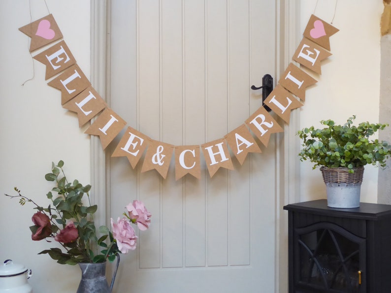 Pu&ograve; includere: Uno striscione in juta con i nomi "Ellie & Charlie" in lettere bianche e cuori rosa su ogni estremit&agrave;.