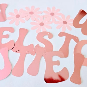 May include: Pink and white paper letters spelling out the word "Welcome" with pink paper flowers.