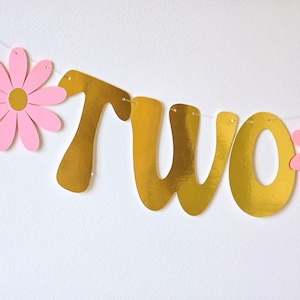 May include: Gold glitter "two" banner with pink paper flowers. The banner is strung with white thread.