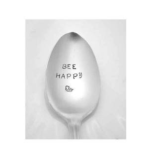 May include: A silver spoon with the words "BEE HAPPY" engraved on it. A small bee design is also engraved on the spoon.