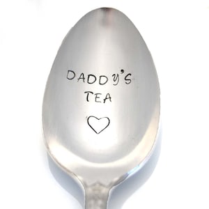 May include: A stainless steel spoon with the words "DADDY'S TEA" and a heart etched into the spoon's bowl. The spoon has a simple, elegant design, perfect for a tea lover.