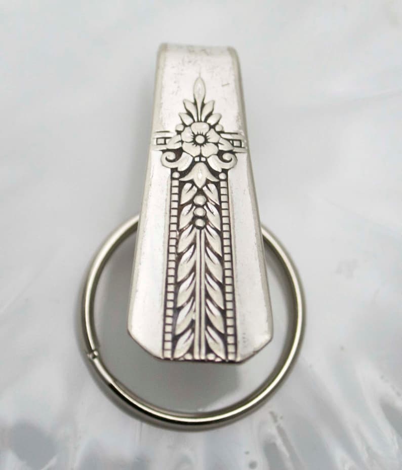 May include: A silver key chain with a decorative spoon charm. The spoon has an ornate design with a flower and leaves.